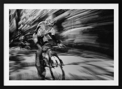 A dramatic black and white action shot of a professional cyclist racing. The cyclist is in focus, wearing a helmet and sunglasses, while the background is a streaky motion blur, creating a powerful sense of speed and movement. The image is enclosed in a silver frame. Wall Art