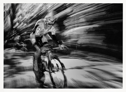 A dramatic black and white action shot of a professional cyclist racing. The cyclist is in focus, wearing a helmet and sunglasses, while the background is a streaky motion blur, creating a powerful sense of speed and movement. The image is enclosed in a silver frame. Wall Art