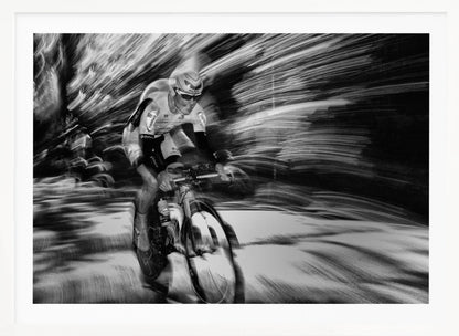 A dramatic black and white action shot of a professional cyclist racing. The cyclist is in focus, wearing a helmet and sunglasses, while the background is a streaky motion blur, creating a powerful sense of speed and movement. The image is enclosed in a silver frame. Wall Art