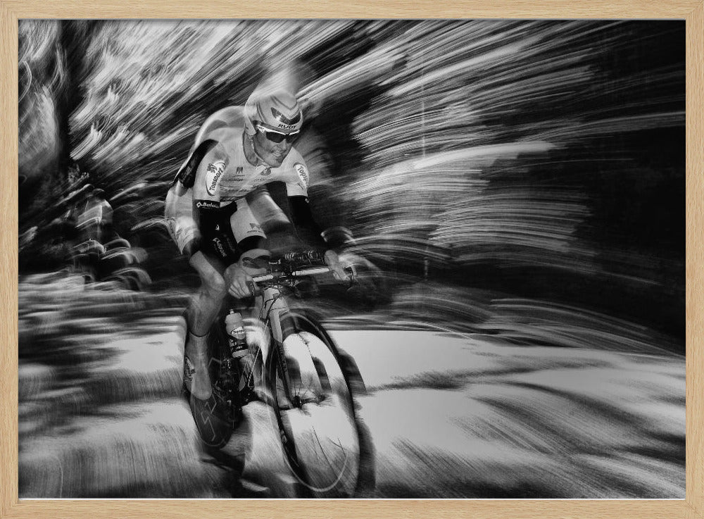 A dramatic black and white action shot of a professional cyclist racing. The cyclist is in focus, wearing a helmet and sunglasses, while the background is a streaky motion blur, creating a powerful sense of speed and movement. The image is enclosed in a silver frame. Wall Art