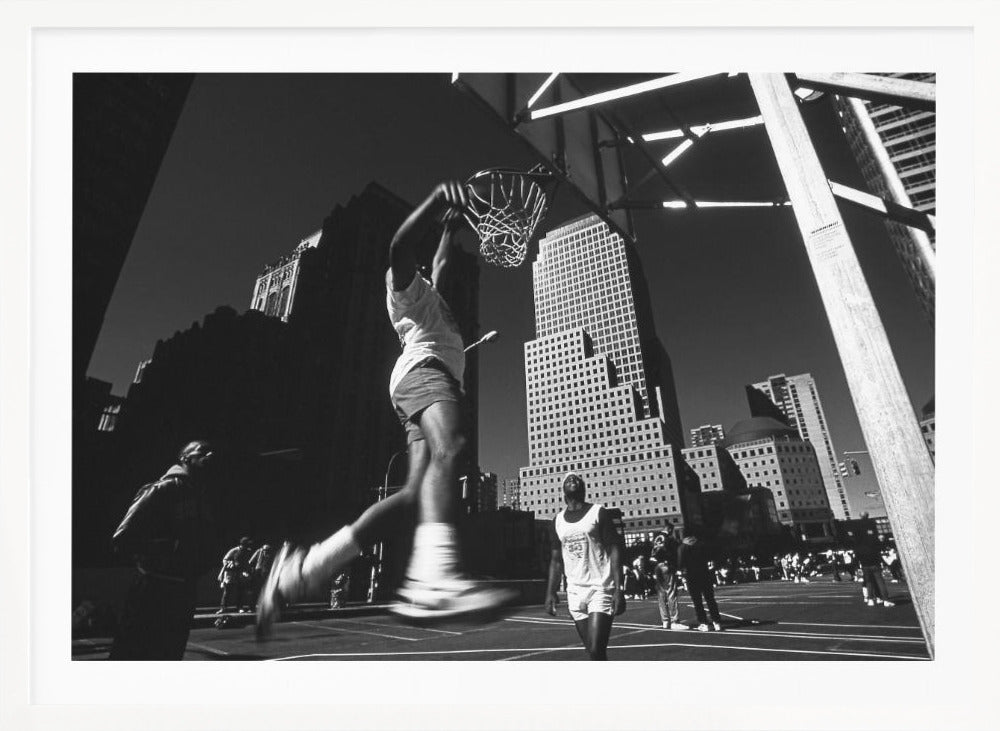 A low-angle, black and white action shot of a person dunking a basketball on an outdoor court, with tall city skyscrapers dominating the background under a clear sky. Print