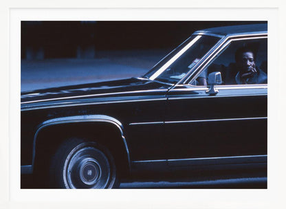 A moody, blue-toned photograph of a Black man sitting pensively in the driver's seat of a dark vintage sedan at night, framed in silver. Poster