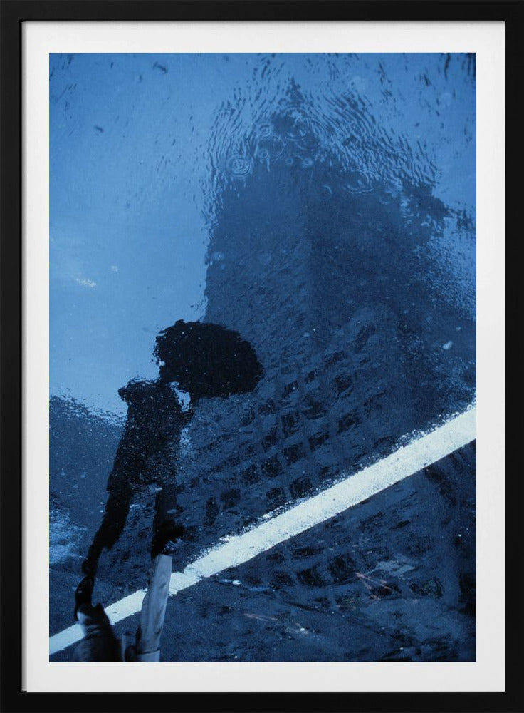 A moody, blue-toned photograph of a reflection in a rainy puddle. A black silhouette of a person holding an umbrella and a distorted brick building are visible, with a single white line crossing the wet street. Poster