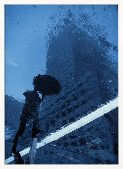 A moody, blue-toned photograph of a reflection in a rainy puddle. A black silhouette of a person holding an umbrella and a distorted brick building are visible, with a single white line crossing the wet street. Poster
