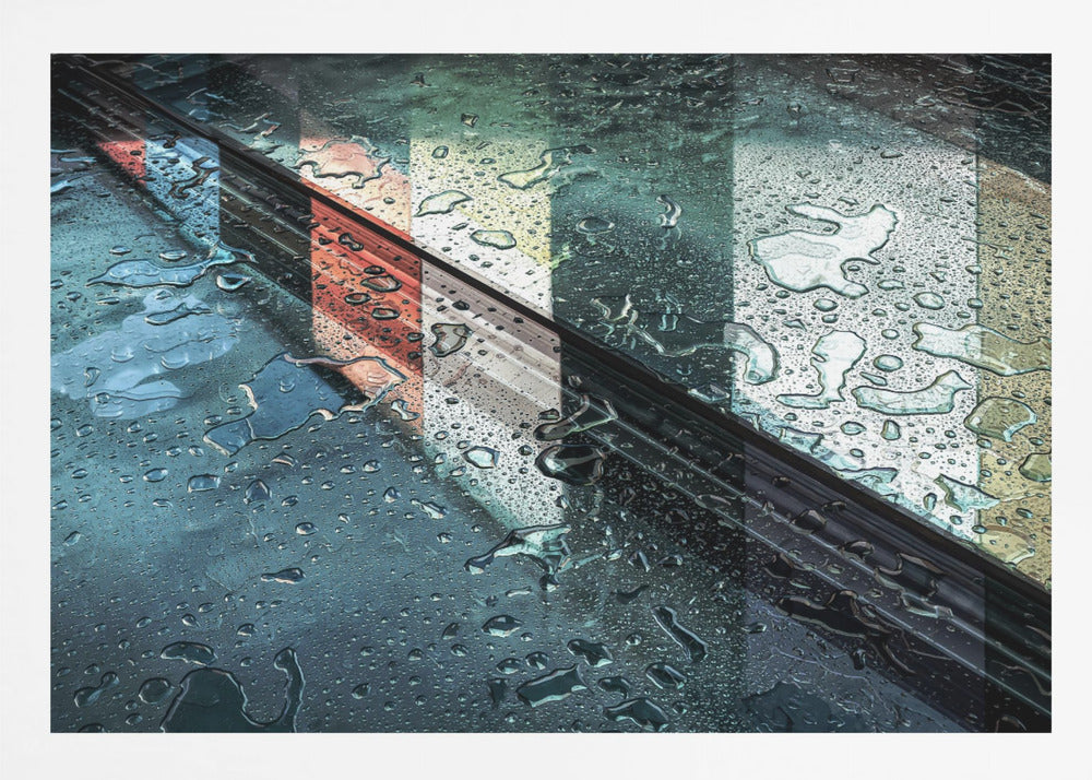 An abstract close-up photograph of a wet, dark surface, possibly a car, covered in raindrops, with a prominent black diagonal line. Colorful vertical stripes of red, cream, and green are reflected on the glossy, wet surface. The artwork is presented in a silver frame. Decor