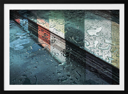 An abstract close-up photograph of a wet, dark surface, possibly a car, covered in raindrops, with a prominent black diagonal line. Colorful vertical stripes of red, cream, and green are reflected on the glossy, wet surface. The artwork is presented in a silver frame. Decor