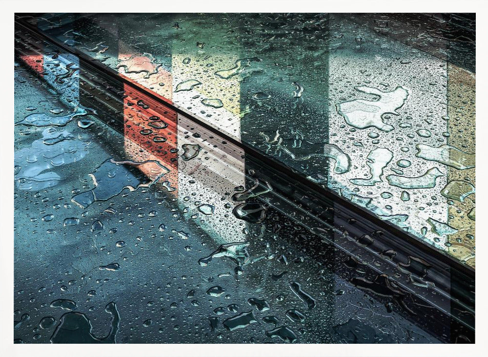 An abstract close-up photograph of a wet, dark surface, possibly a car, covered in raindrops, with a prominent black diagonal line. Colorful vertical stripes of red, cream, and green are reflected on the glossy, wet surface. The artwork is presented in a silver frame. Decor