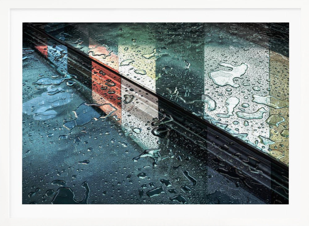 An abstract close-up photograph of a wet, dark surface, possibly a car, covered in raindrops, with a prominent black diagonal line. Colorful vertical stripes of red, cream, and green are reflected on the glossy, wet surface. The artwork is presented in a silver frame. Decor