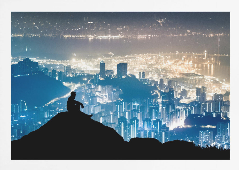 A silhouette of a person sitting on a hilltop, gazing out over a vast, illuminated city skyline at night. The city lights glow in shades of blue and gold against the dark landscape, with a body of water in the distance. Decor