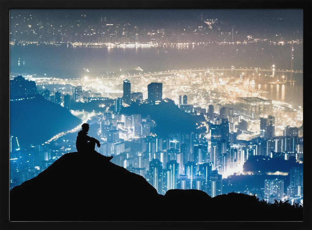 A silhouette of a person sitting on a hilltop, gazing out over a vast, illuminated city skyline at night. The city lights glow in shades of blue and gold against the dark landscape, with a body of water in the distance. Decor