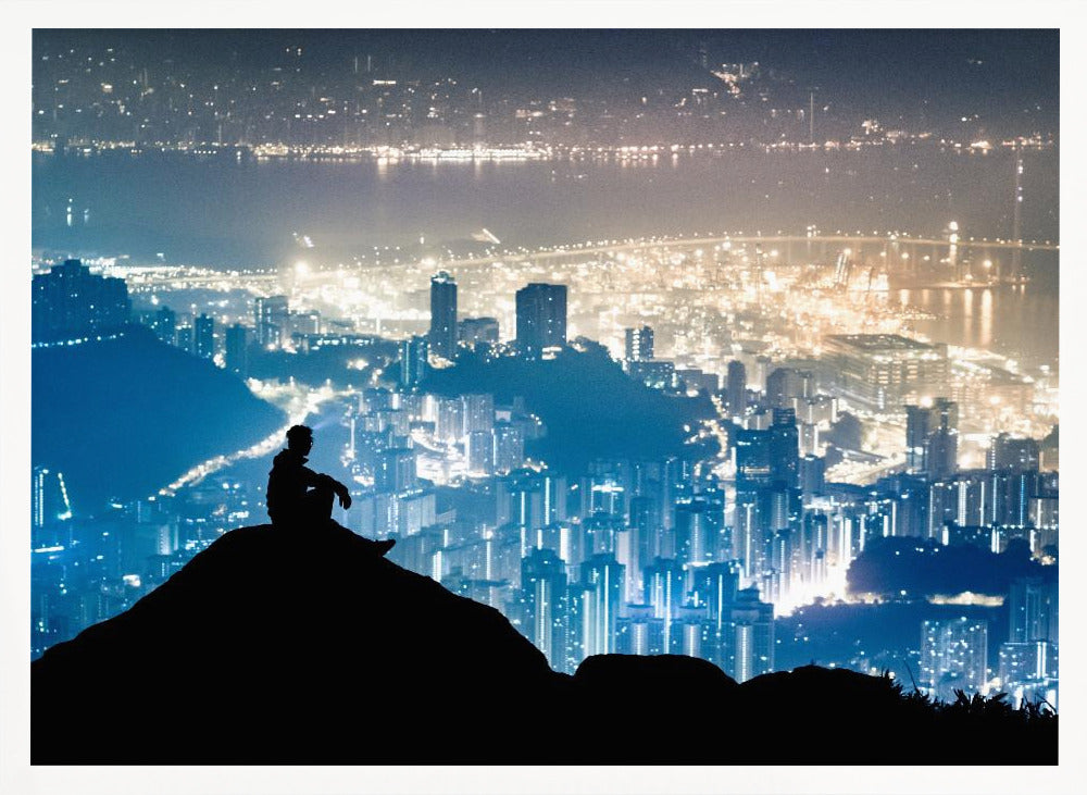 A silhouette of a person sitting on a hilltop, gazing out over a vast, illuminated city skyline at night. The city lights glow in shades of blue and gold against the dark landscape, with a body of water in the distance. Decor