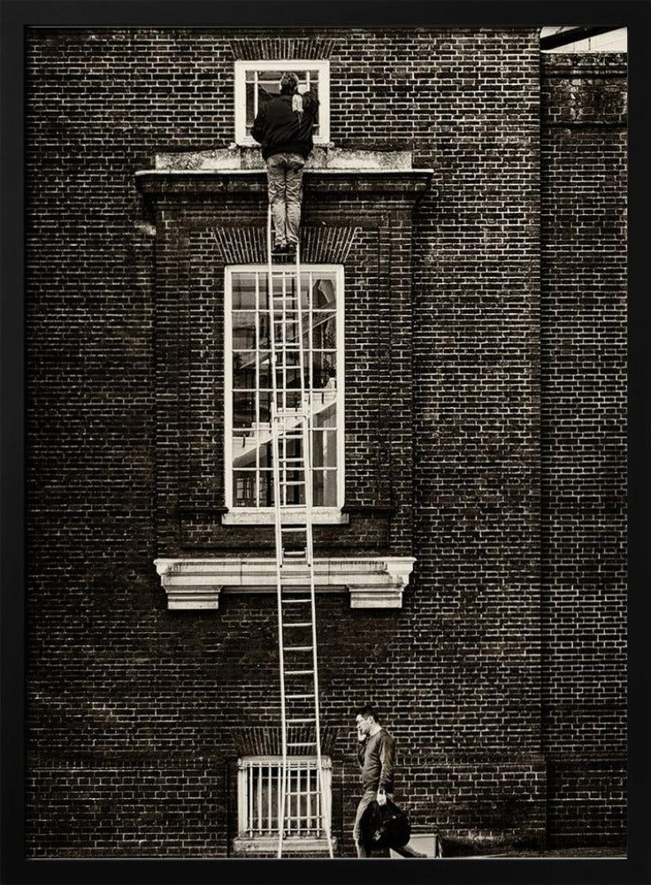 A striking black and white photograph of a man cleaning a small window high up on a brick building, standing precariously at the top of a very long ladder. Below, another man walks past on the street, seemingly unaware of the scene above. Artwork