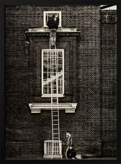 A striking black and white photograph of a man cleaning a small window high up on a brick building, standing precariously at the top of a very long ladder. Below, another man walks past on the street, seemingly unaware of the scene above. Artwork