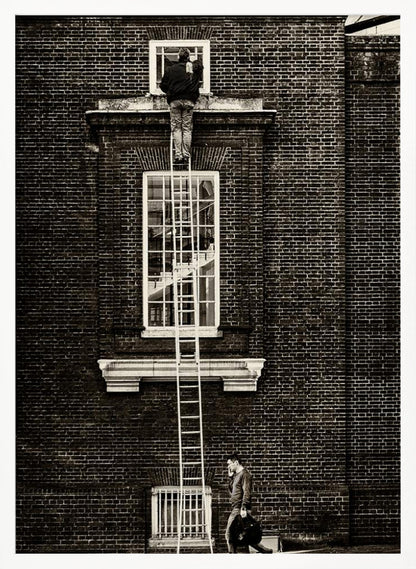 A striking black and white photograph of a man cleaning a small window high up on a brick building, standing precariously at the top of a very long ladder. Below, another man walks past on the street, seemingly unaware of the scene above. Artwork