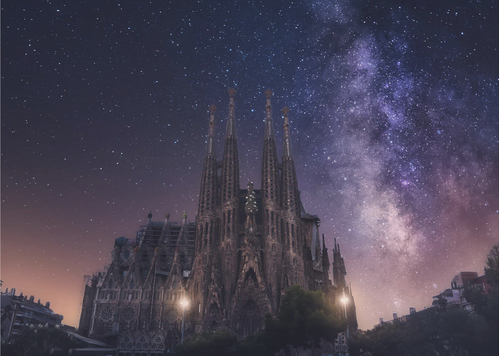 A fantastical night view of the Sagrada Familia in Barcelona, its intricate spires reaching up towards a magnificent, starry sky filled with the purple and pink hues of the Milky Way galaxy, all enclosed in a silver frame. Artwork