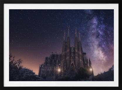 A fantastical night view of the Sagrada Familia in Barcelona, its intricate spires reaching up towards a magnificent, starry sky filled with the purple and pink hues of the Milky Way galaxy, all enclosed in a silver frame. Artwork