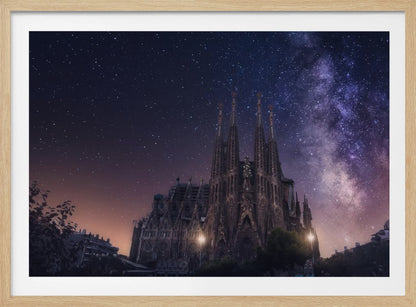 A fantastical night view of the Sagrada Familia in Barcelona, its intricate spires reaching up towards a magnificent, starry sky filled with the purple and pink hues of the Milky Way galaxy, all enclosed in a silver frame. Artwork