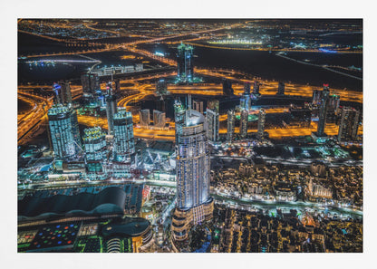 An aerial nighttime photograph of a sprawling modern city, possibly Dubai, with brightly lit skyscrapers and a complex network of illuminated highways creating a vibrant contrast against the dark landscape, all enclosed in a silver frame. Decor