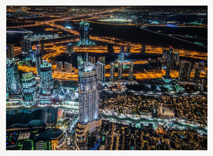 An aerial nighttime photograph of a sprawling modern city, possibly Dubai, with brightly lit skyscrapers and a complex network of illuminated highways creating a vibrant contrast against the dark landscape, all enclosed in a silver frame. Decor