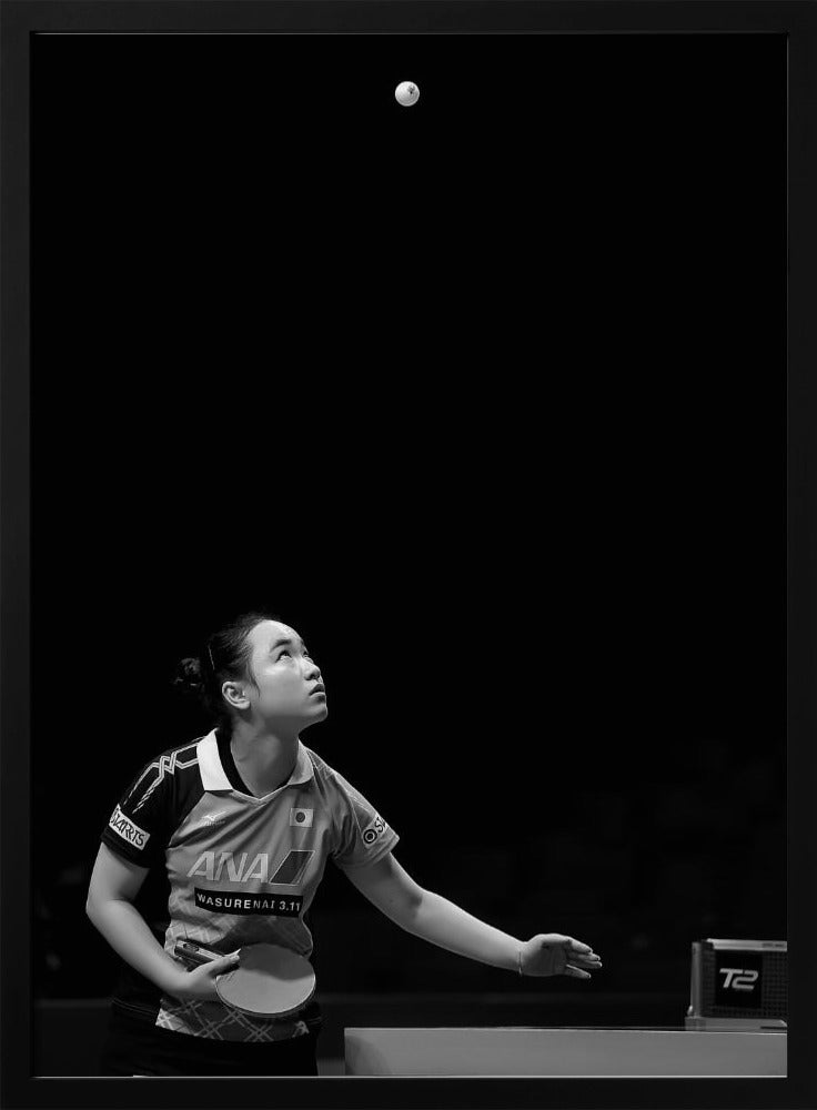 A dramatic black and white vertical photograph of a female table tennis player mid-serve. Positioned in the lower-left, she looks up with intense focus at the white ball suspended high in the air against a solid black background. Poster