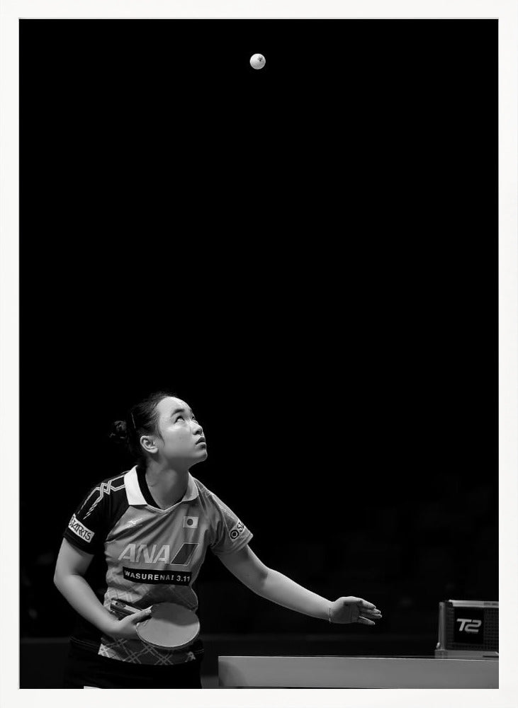 A dramatic black and white vertical photograph of a female table tennis player mid-serve. Positioned in the lower-left, she looks up with intense focus at the white ball suspended high in the air against a solid black background. Poster