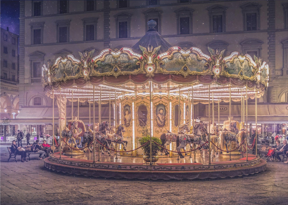 A beautifully illuminated vintage carousel with ornate horses in a European cobblestone plaza at night. The carousel is the central focus, glowing with warm lights against a backdrop of historic buildings and a starry purple sky. Poster