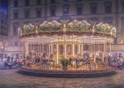 A beautifully illuminated vintage carousel with ornate horses in a European cobblestone plaza at night. The carousel is the central focus, glowing with warm lights against a backdrop of historic buildings and a starry purple sky. Poster
