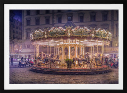 A beautifully illuminated vintage carousel with ornate horses in a European cobblestone plaza at night. The carousel is the central focus, glowing with warm lights against a backdrop of historic buildings and a starry purple sky. Poster