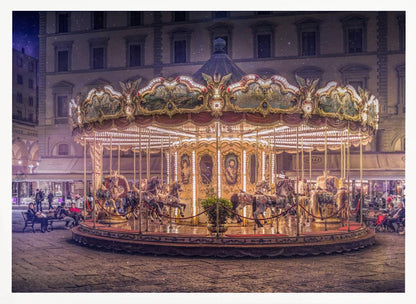 A beautifully illuminated vintage carousel with ornate horses in a European cobblestone plaza at night. The carousel is the central focus, glowing with warm lights against a backdrop of historic buildings and a starry purple sky. Poster