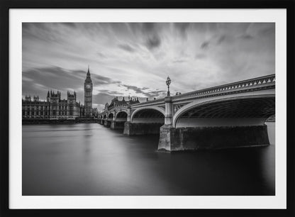 A dramatic black and white long-exposure photograph of London, featuring the smooth River Thames in the foreground, Westminster Bridge on the right, and the iconic Big Ben and Houses of Parliament on the left under a cloudy, streaked sky. The image is presented in a silver frame. Print