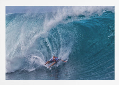 A dramatic action shot of a professional surfer skillfully navigating the inside of a massive, curling blue ocean wave, surrounded by white sea spray, all enclosed in a silver frame. Artwork
