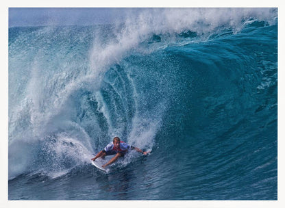 A dramatic action shot of a professional surfer skillfully navigating the inside of a massive, curling blue ocean wave, surrounded by white sea spray, all enclosed in a silver frame. Artwork