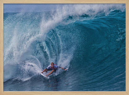 A dramatic action shot of a professional surfer skillfully navigating the inside of a massive, curling blue ocean wave, surrounded by white sea spray, all enclosed in a silver frame. Artwork