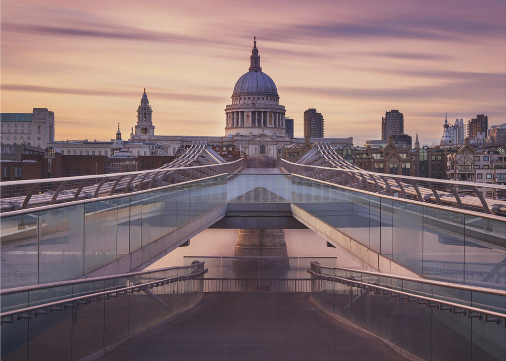 A photograph looking down the center of the Millennium Bridge in London, leading the eye directly to St. Paul's Cathedral, which is centered in the background under a beautiful purple and orange sunset sky. Print