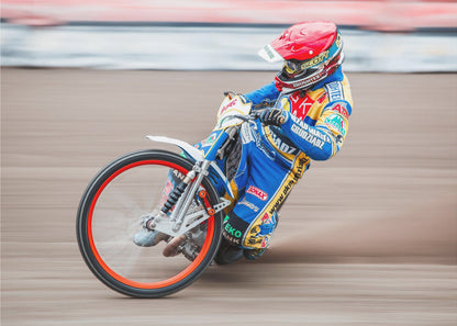 A speedway motorcycle racer in a blue and yellow suit with a red helmet leans sharply into a turn on a dirt track, with motion blur in the background conveying a sense of high speed. Print