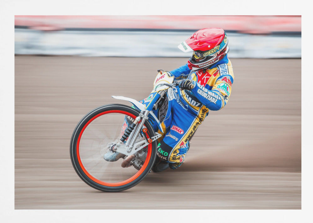 A speedway motorcycle racer in a blue and yellow suit with a red helmet leans sharply into a turn on a dirt track, with motion blur in the background conveying a sense of high speed. Print