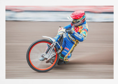 A speedway motorcycle racer in a blue and yellow suit with a red helmet leans sharply into a turn on a dirt track, with motion blur in the background conveying a sense of high speed. Print