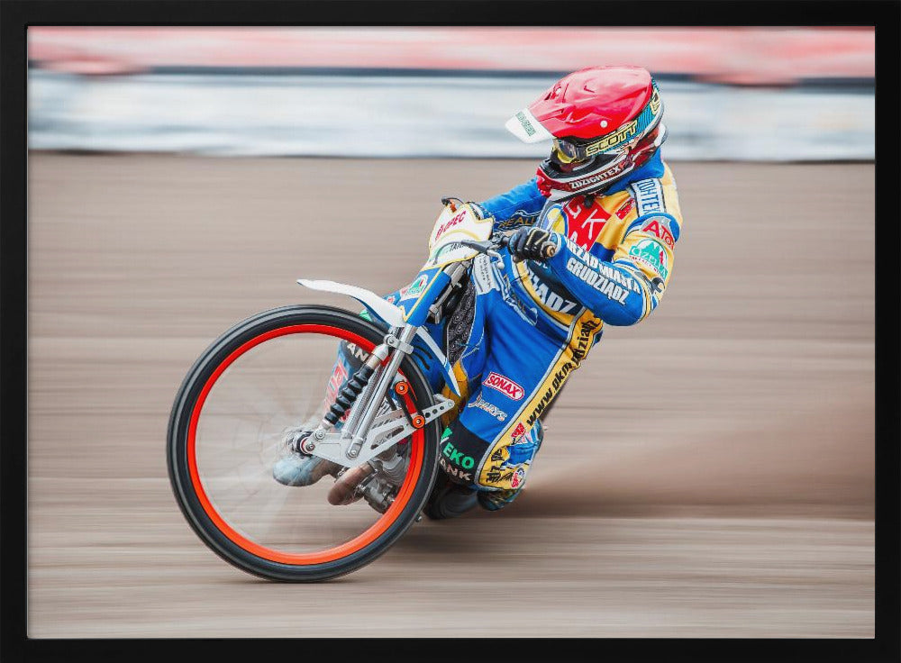 A speedway motorcycle racer in a blue and yellow suit with a red helmet leans sharply into a turn on a dirt track, with motion blur in the background conveying a sense of high speed. Print