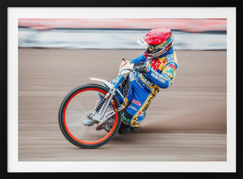 A speedway motorcycle racer in a blue and yellow suit with a red helmet leans sharply into a turn on a dirt track, with motion blur in the background conveying a sense of high speed. Print