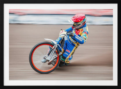 A speedway motorcycle racer in a blue and yellow suit with a red helmet leans sharply into a turn on a dirt track, with motion blur in the background conveying a sense of high speed. Print