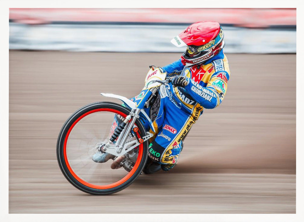 A speedway motorcycle racer in a blue and yellow suit with a red helmet leans sharply into a turn on a dirt track, with motion blur in the background conveying a sense of high speed. Print