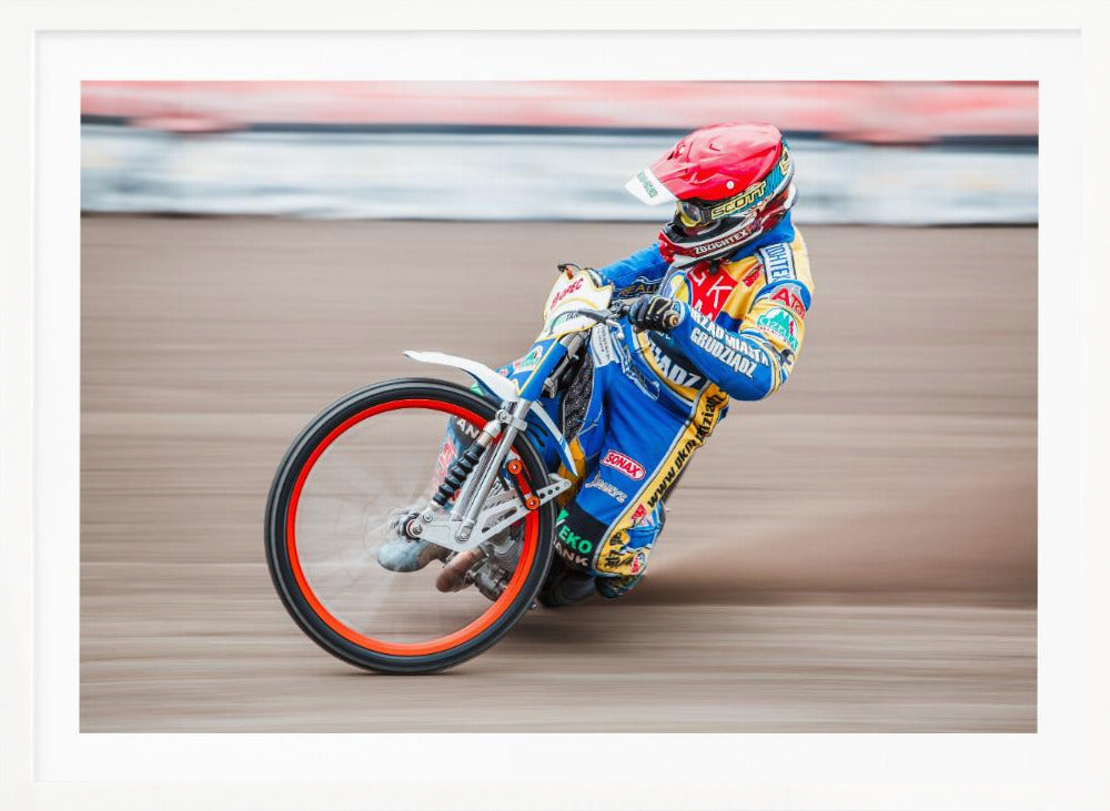 A speedway motorcycle racer in a blue and yellow suit with a red helmet leans sharply into a turn on a dirt track, with motion blur in the background conveying a sense of high speed. Print