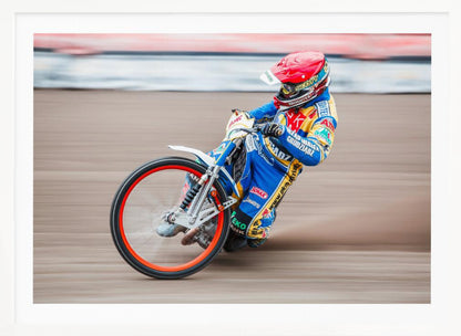 A speedway motorcycle racer in a blue and yellow suit with a red helmet leans sharply into a turn on a dirt track, with motion blur in the background conveying a sense of high speed. Print