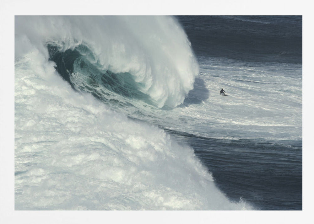 A framed aerial photograph captures a dramatic ocean scene where a lone surfer on a surfboard is dwarfed by an immense, powerful wave cresting nearby, conveying a sense of scale and adventure. Artwork