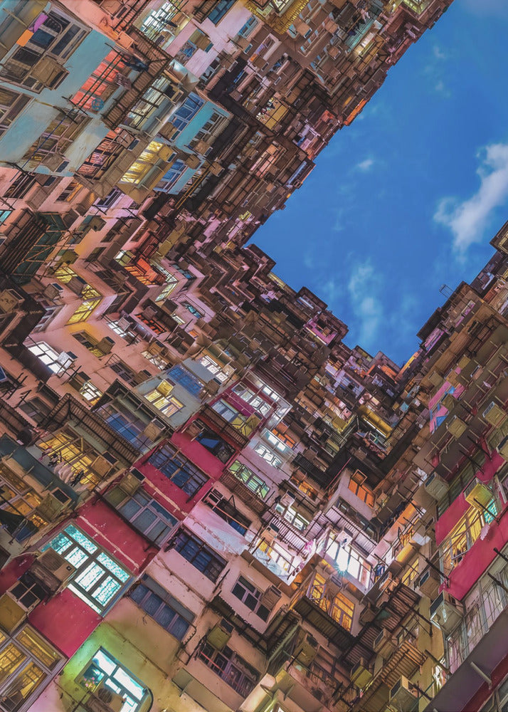 A dramatic worm's-eye view looking up at colorful, densely packed high-rise apartment buildings that create a geometric frame around a patch of deep blue sky. Wall Art