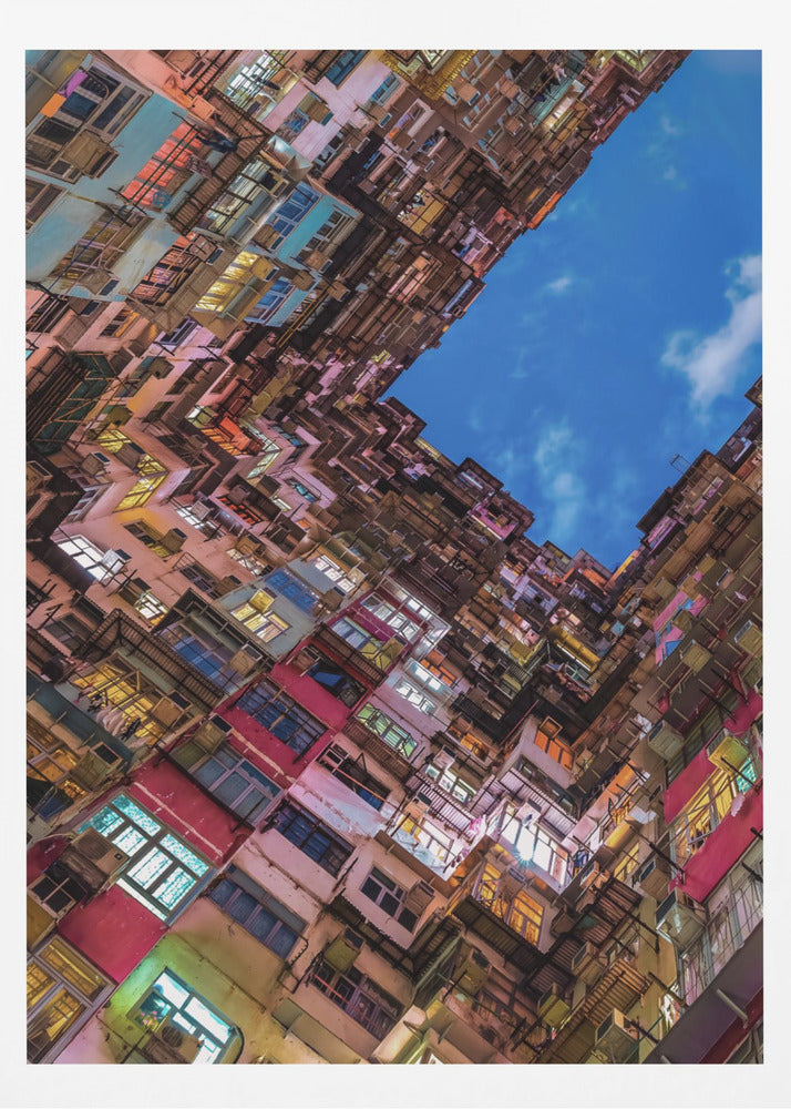 A dramatic worm's-eye view looking up at colorful, densely packed high-rise apartment buildings that create a geometric frame around a patch of deep blue sky. Wall Art