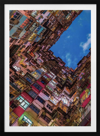 A dramatic worm's-eye view looking up at colorful, densely packed high-rise apartment buildings that create a geometric frame around a patch of deep blue sky. Wall Art