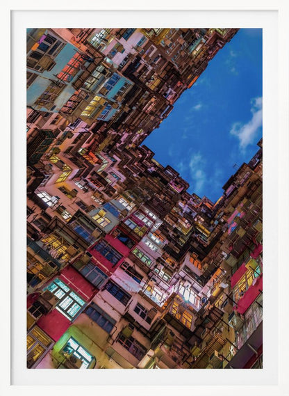 A dramatic worm's-eye view looking up at colorful, densely packed high-rise apartment buildings that create a geometric frame around a patch of deep blue sky. Wall Art