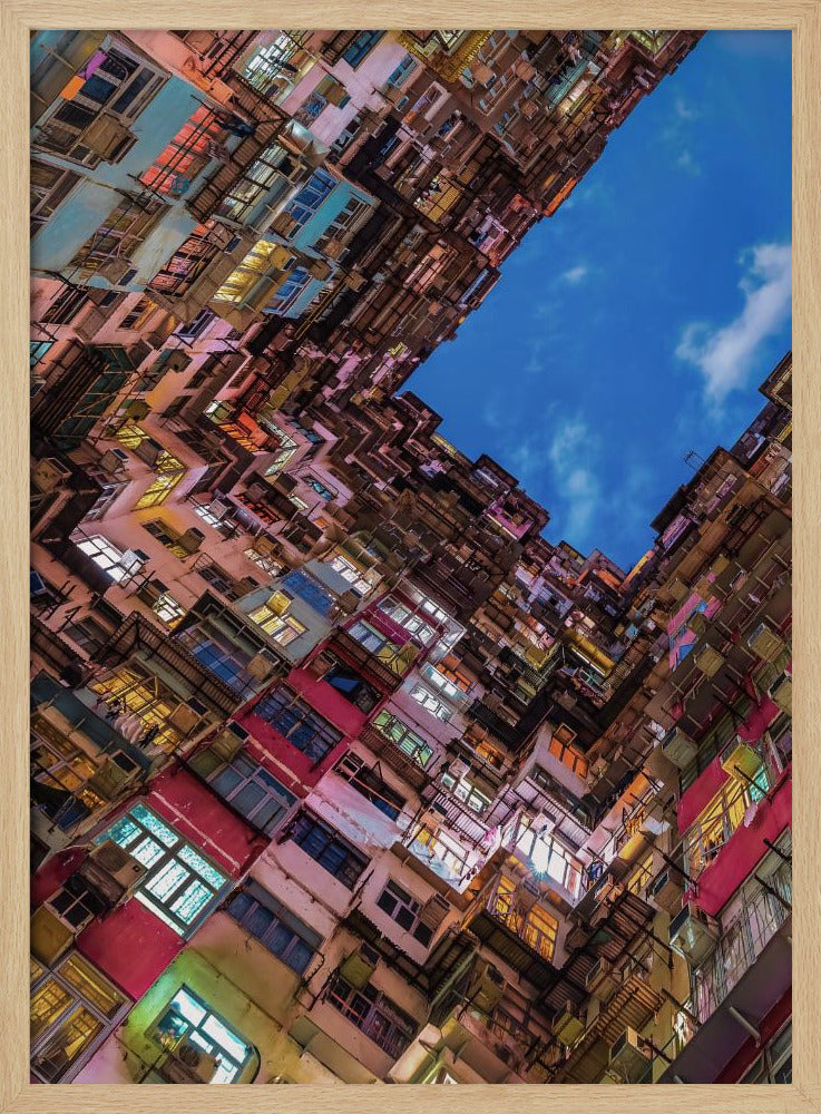 A dramatic worm's-eye view looking up at colorful, densely packed high-rise apartment buildings that create a geometric frame around a patch of deep blue sky. Wall Art