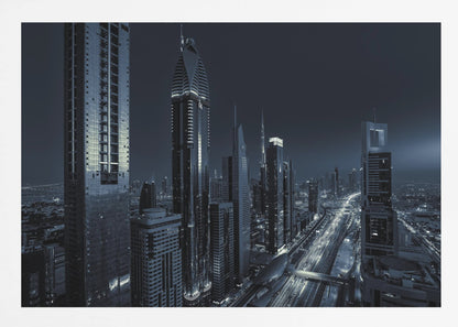 A framed, blue-toned nighttime photograph of a futuristic city skyline from an elevated perspective, featuring illuminated skyscrapers and light trails from traffic on a major highway stretching into the distance. Poster
